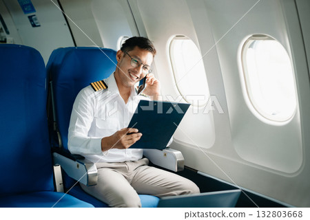 Asian Confident male pilot in uniform leaning at the passenger seat while standing inside of the airplane flight cockpit during takeof 132803668