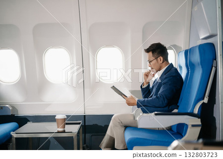 Young Asian executive excels in first class, multitasking with digital tablet, laptop and smartphone. Travel in style, 132803723