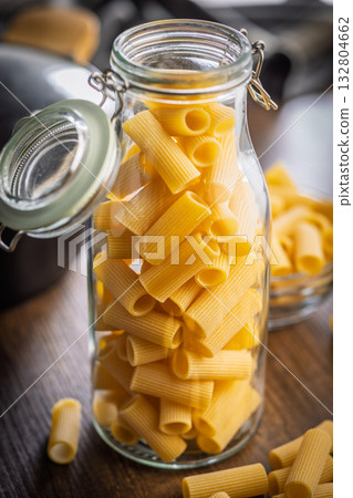 Uncooked rigatoni pasta in jar on wooden table. 132804662