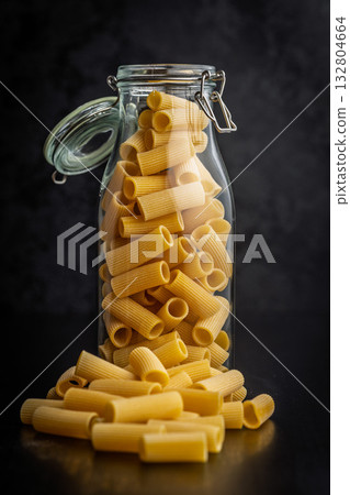 Uncooked rigatoni pasta in jar on black table. Uncooked rigatoni pasta in jar on black table. 132804664