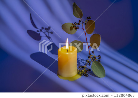 Atmospheric still life with a yellow candle, a eucalyptus branch and berries on a lilac-purple background. 132804863