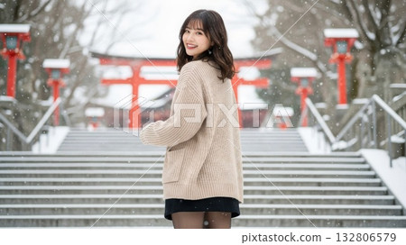 一位身穿針織毛衣和裙子的女子回頭望向白雪皚皚的神社，露出微笑。 132806579