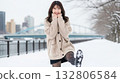 A woman in a knitted sweater and skirt raising one leg on a snowy riverbank 132806584