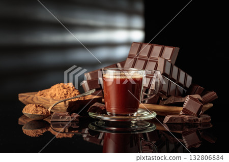 Mug of hot chocolate against broken bitter chocolate bars and dish with cocoa powder. Mug of hot chocolate against broken bitter chocolate bars and dish with cocoa powder. 132806884