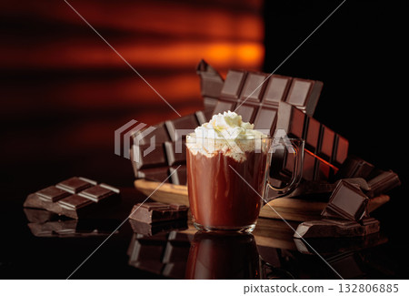 A mug of hot chocolate with whipped cream against broken bitter chocolate bars. A mug of hot chocolate with whipped cream against broken bitter chocolate bars. 132806885