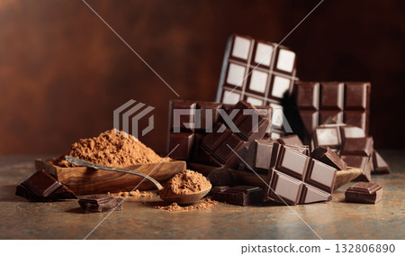 Scraps of dark chocolate next to a wooden bowl of cocoa powder. Scraps of dark chocolate next to a wooden bowl of cocoa powder. 132806890