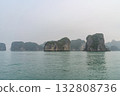 Stunning view of limestone karsts rising majestically from tranquil waters in Ha Long Bay, Vietnam. Lush greenery covers the islands under a serene, misty sky. 132808736