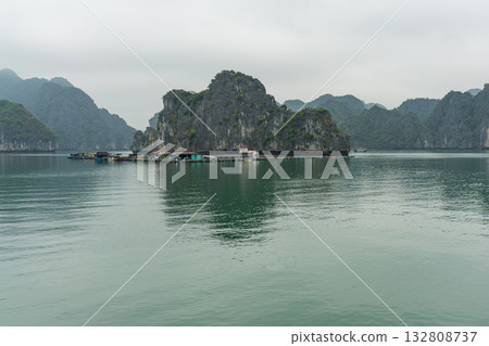 A serene view of the iconic Ha Long Bay, showcasing floating villages, limestone karsts, and calm waters under a cloudy sky. A serene view of the iconic Ha Long Bay, showcasing floating villages, limestone karsts, and calm waters under a cloudy sky. 132808737