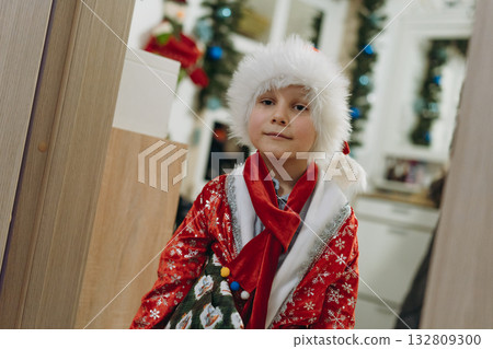 cute little boy wearing santa costume and hat at home holding christmas gift 132809300