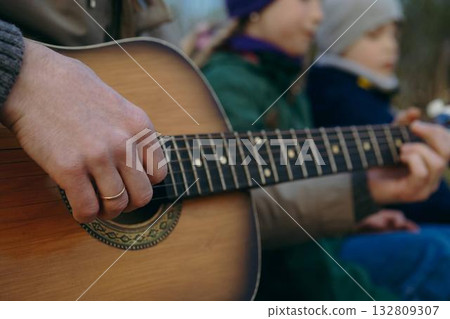 close up view of man's hands playing an acoustic guitar.children on background. Autumn family picnic 132809307