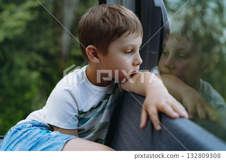 A thoughtful young boy sitting in a funicular cabin, looking out the window with a contemplative expression 132809308