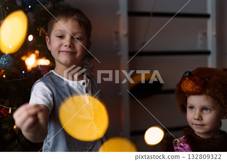 Two children are holding burning sparklers with looks of awe and joy on their faces 132809322