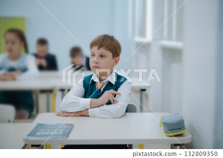 8 years old boy wearning green uniform vest and white shirt sitting at the class in school. 132809350