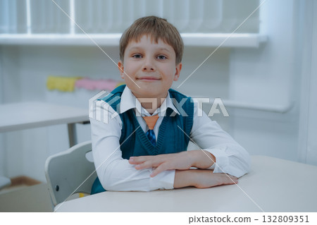 cute little boy wearning green uniform vest and white shirt sitting at the class in school. 132809351