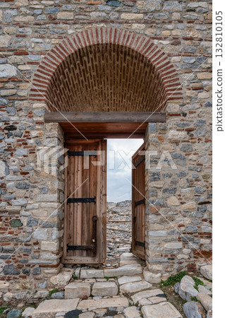Historic Fortress Entrance: Stone and Brick Wall with Arched Doorway and Open Wooden Gate to Rocky Path Historic Fortress Entrance: Stone and Brick Wall with Arched Doorway and Open Wooden Gate to Rocky Path 132810105