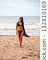 A confident woman strolls along the beach, showcasing her vibrant summer style and relaxation vibes 132810169