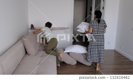 A boy and his mother arrange cushions and pillows together in a bright living room, captured naturally from a side view. The photo highlights teamwork, discipline, and shared responsibility in A boy and his mother arrange cushions and pillows together in a bright living room, captured naturally from a side view. The photo highlights teamwork, discipline, and shared responsibility in 132810462
