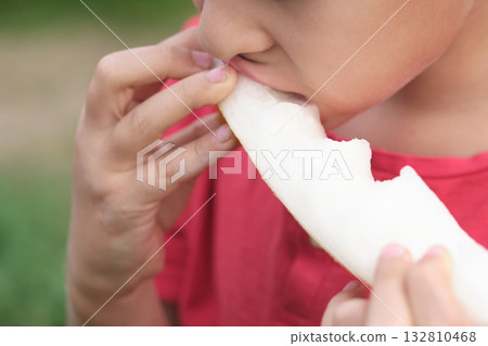 Detailed shot capturing a child's delight in biting into a juicy melon, highlighting the textures and vivid colors. Promotes the joy of eating seasonal fruits. Detailed shot capturing a child's delight in biting into a juicy melon, highlighting the textures and vivid colors. Promotes the joy of eating seasonal fruits. 132810468