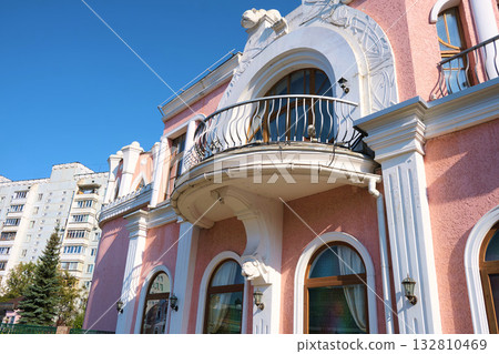 Elegant classical-style building with pink stucco walls, white decorative columns, and arched windows, featuring a curved balcony with wrought iron railings. The image highlights architectural Elegant classical-style building with pink stucco walls, white decorative columns, and arched windows, featuring a curved balcony with wrought iron railings. The image highlights architectural 132810469