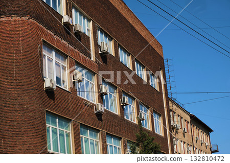 Old industrial brick building with glass block stairwell and multiple external air conditioning units mounted along the facade. The photo illustrates urban infrastructure aging, facade maintenance Old industrial brick building with glass block stairwell and multiple external air conditioning units mounted along the facade. The photo illustrates urban infrastructure aging, facade maintenance 132810472