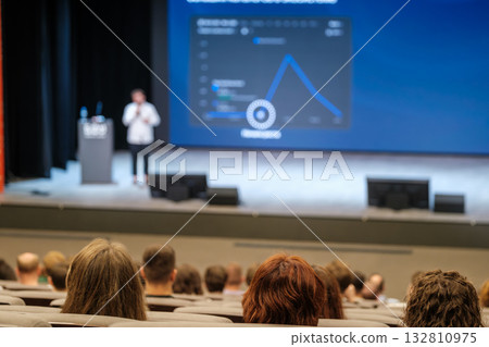 Conference presentation with speaker on stage and large screen displaying chart for audience 132810975