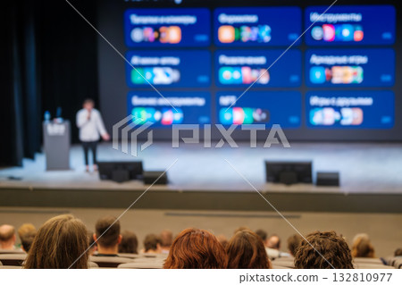 Conference presentation in a large auditorium with a speaker and audience listening attentively 132810977