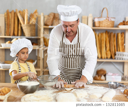 Little daughter and father make dough together in bakery kitchen Little daughter and father make dough together in bakery kitchen 132811085