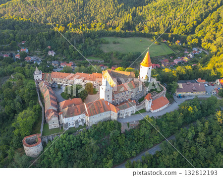 Krivoklat Castle stands majestically amid lush greenery, captured from above during a beautiful sunset. This medieval structure showcases rich history and stunning architecture in Central Bohemia. 132812193