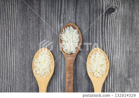 Raw white rice on wooden background. Long uncooked rice in wooden plate. Natural organic food. Traditional Asian cereal culture. Raw white rice on wooden background. Long uncooked rice in wooden plate. Natural organic food. Traditional Asian cereal culture. 132814329