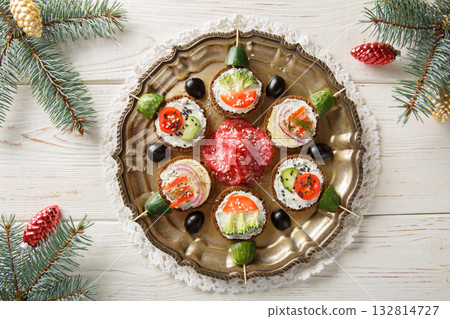 Christmas sandwiches snack in the form of New Year's balls with cream cheese and fresh vegetables close-up in a plate on the table. Horizontal top view 132814727