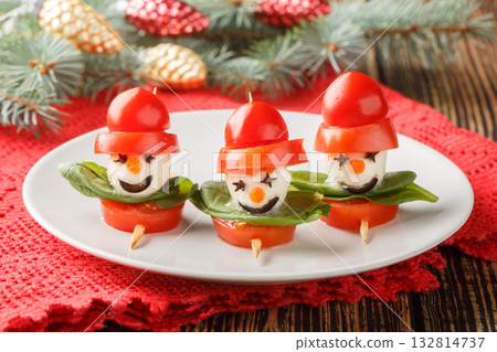 Christmas Appetizer Snowmen made of mozzarella, tomatoes and basil on skewers close-up in a plate. Horizontal 132814737