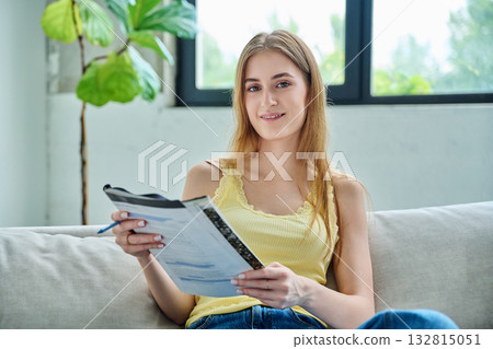 Young student girl study online, sitting at home on couch with textbook Young student girl study online, sitting at home on couch with textbook 132815051