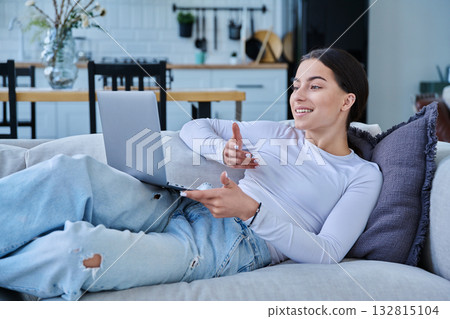 Young teenage girl using laptop for video chat lying on sofa at home 132815104