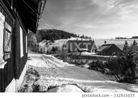 Winter sunlight brightens Jizerka village on a serene morning. Snow blankets the ground as charming cottages stand amidst a pine forest, creating a peaceful atmosphere. Winter sunlight brightens Jizerka village on a serene morning. Snow blankets the ground as charming cottages stand amidst a pine forest, creating a peaceful atmosphere. 132815835