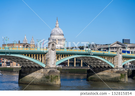 Southwalk Bridge stands tall over the River Thames on a clear sunny day. The iconic structure connects the banks of London, showcasing its unique architecture and lively surroundings. Southwalk Bridge stands tall over the River Thames on a clear sunny day. The iconic structure connects the banks of London, showcasing its unique architecture and lively surroundings. 132815854