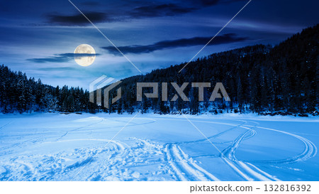 winter landscape with snow covered ground at night. mountains with frozen lake among spruce forest in full moon light. scenic view of winter wonderland. background for investment or abstract concepts winter landscape with snow covered ground at night. mountains with frozen lake among spruce forest in full moon light. scenic view of winter wonderland. background for investment or abstract concepts 132816392