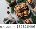 Flat lay of homemade mince pies with Christmas decorations, star anise, pine branches, wrapped gifts on gray stone background 132816406