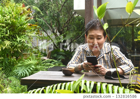 elder woman enjoy to drinking coffee read book and used mobile phone in cafe garden on afternoon elder woman enjoy to drinking coffee read book and used mobile phone in cafe garden on afternoon 132816586
