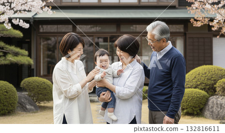 A three-generation family smiling and surrounding a baby in front of their house 132816611