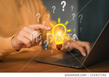 Creative thinking and innovation concept. A glowing light bulb surrounded by question marks with a person pointing toward it while using a laptop, symbolizing problem solving, ideas and brainstorming. Creative thinking and innovation concept. A glowing light bulb surrounded by question marks with a person pointing toward it while using a laptop, symbolizing problem solving, ideas and brainstorming. 132817102