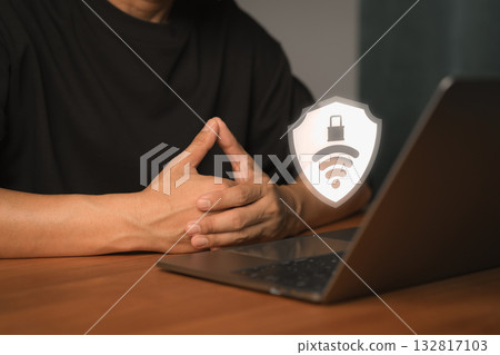 Cybersecurity and WiFi protection concept. A shield with a lock and wireless symbol on laptop computer with a person sitting behind it, symbolizing secure internet, data privacy and online safety. 132817103