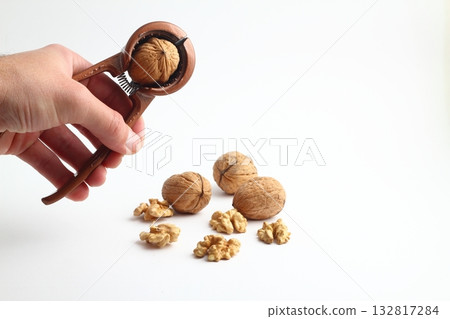 Nutcracker held in male hand and crack a walnut isolated on a white background. Nutcracker held in male hand and crack a walnut isolated on a white background. 132817284