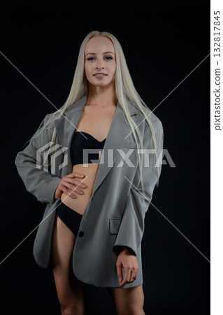 Model in oversized blazer and bikini posing confidently against a dark backdrop 132817845
