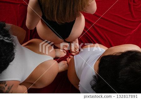 Sensual moment captured with three women in elegant lingerie on rich red fabric 132817891