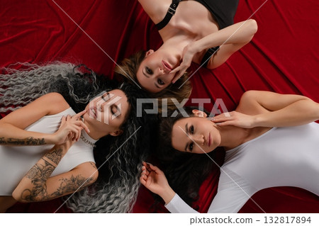 Three women showcase beauty and sensuality in elegant lingerie on red fabric 132817894