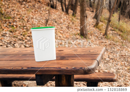 white container with a green lid on a wooden table in an autumn forest, mockup 132818869