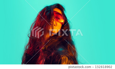 Fashion portrait of woman in visor with flowing hair under neon turquoise glow 132818902