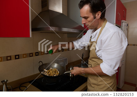 Man In Kitchen Cooking With Apron Stir-Frying Vegetables On Stove 132820153