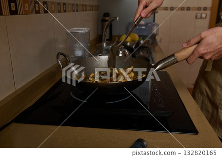 Father Cooking in Wok Pan on Induction Stove While Daughter Helps Prepare Family Dinner Father Cooking in Wok Pan on Induction Stove While Daughter Helps Prepare Family Dinner 132820165
