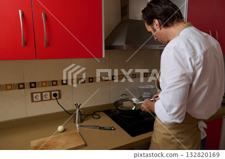 Father Cooking Dinner In Modern Red Kitchen While Preparing Food At The Stove Father Cooking Dinner In Modern Red Kitchen While Preparing Food At The Stove 132820169